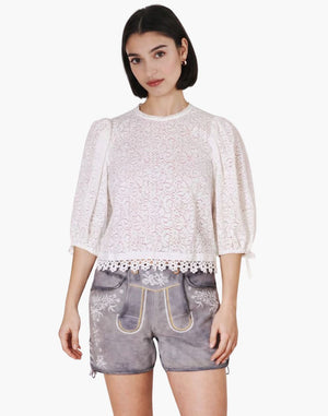 Woman wearing a white lace top and denim shorts on a white background