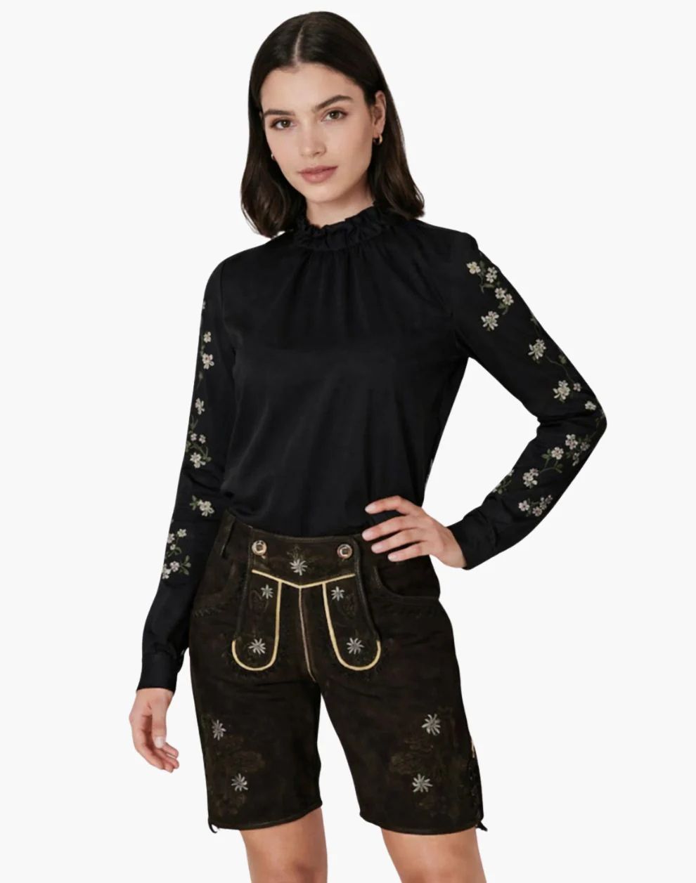 Woman wearing a black long-sleeve top with floral embroidery and black shorts with gold accents on a white background