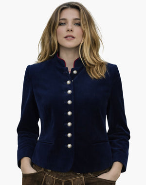 Woman wearing a Bavarian festival Trachten jacket in navy blue with a high collar, pearl-style buttons, and fitted traditional design, paired with brown lederhosen, against a white background.