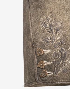 Close-up of brown leather women’s lederhosen showing traditional embroidered floral design and decorative side buttons on a textured distressed leather finish.