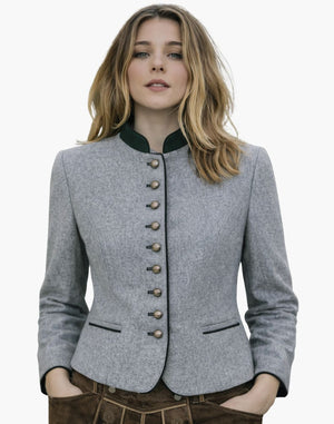 Woman wearing a classic German Trachten jacket in light grey with a green collar, decorative buttons, and fitted traditional Bavarian design, paired with brown lederhosen, against a white background.