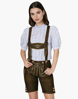 Woman wearing embroidered brown leather lederhosen shorts with a blue shirt , styled in traditional Bavarian Oktoberfest fashion.