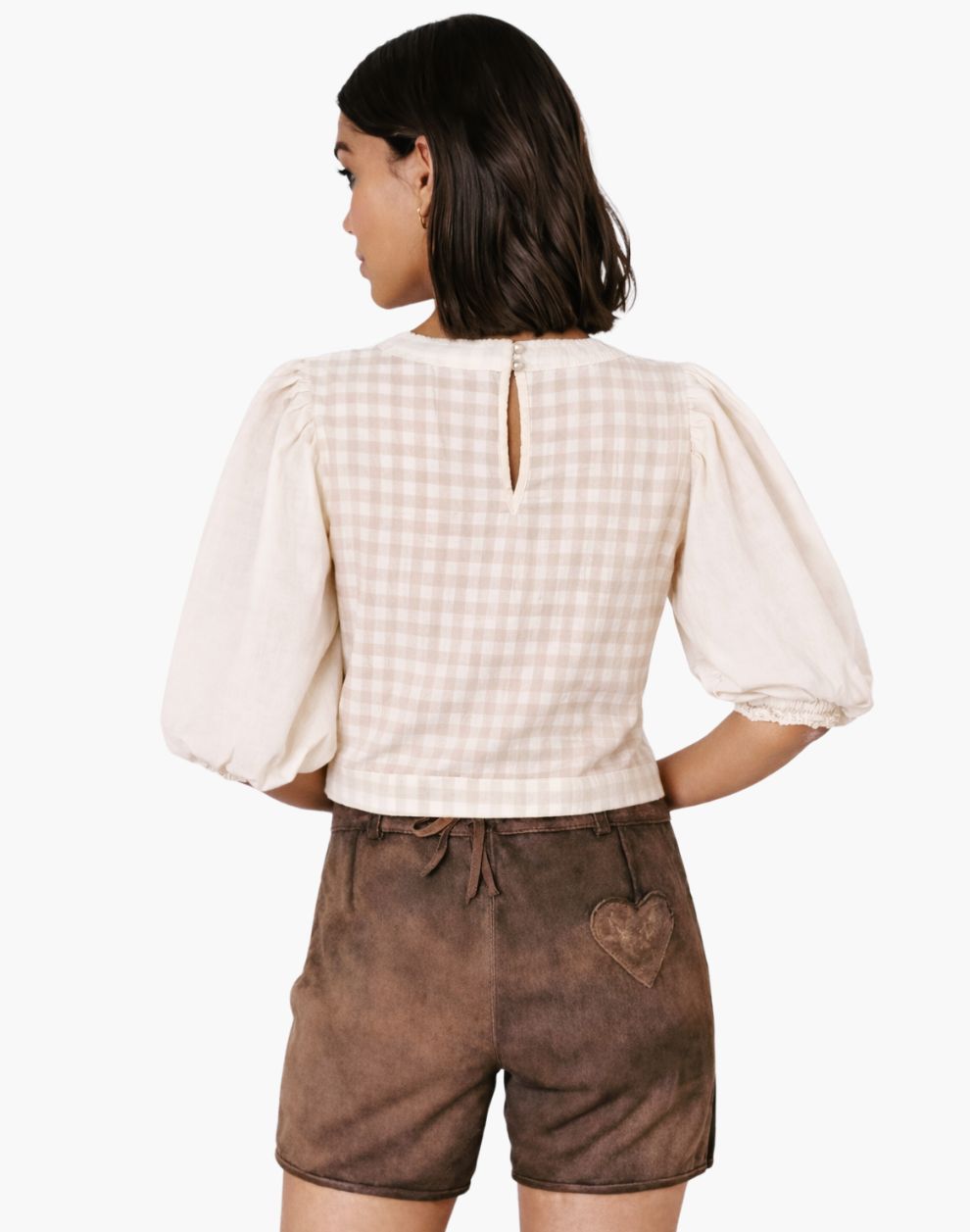 Woman wearing a beige checkered top and brown shorts on a white background