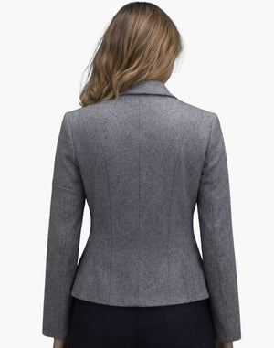 Back view of a woman wearing a fitted light gray wool jacket with structured vertical seams that contour the waist and a slightly flared hem. The tailored jacket is paired with dark trousers, and her shoulder-length blonde hair falls naturally over the collar. The background is plain light gray in a studio setting.
