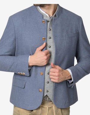 Angled view of model wearing blue wool alpine jacket paired with lederhosen showing classic Bavarian festival style.