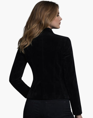 Back view of a woman wearing a black velvet fitted jacket with a structured silhouette, paired with dark pants.
