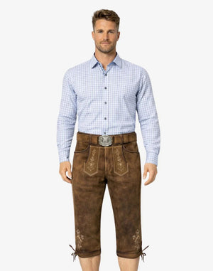Man wearing a light blue checkered shirt and brown traditional pants on a white background