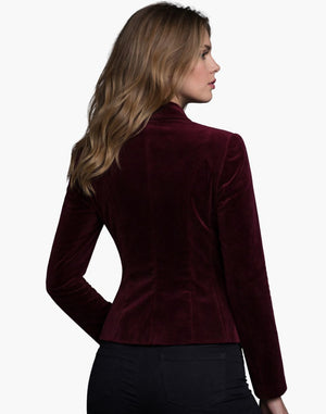 Rear view of a woman wearing a burgundy velvet fitted jacket with a structured silhouette, paired with dark jeans.