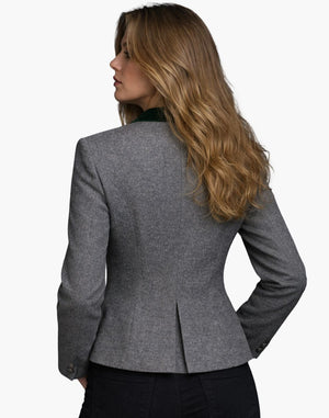 Back view of a woman wearing the same fitted gray wool jacket, showing structured seams that contour the waist and a small center back vent. The collar has a dark green accent, and she pairs the jacket with dark jeans. Her shoulder-length blonde hair falls loosely over the collar. The background is plain light gray.