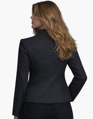 Back view of a woman wearing the same dark charcoal fitted jacket, showing contoured seam lines and a gently flared hem over dark jeans. Her shoulder-length blonde hair falls loosely over the collar. The background is plain light gray, creating a simple studio look.