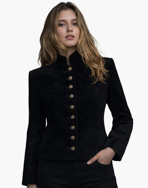 Front view of a woman wearing a black tailored jacket with a stand-up collar and a vertical row of decorative gold-tone buttons down the front. The jacket features subtle welt pockets and a gently flared hem, paired with dark jeans. The background is plain light gray, creating a clean studio look.