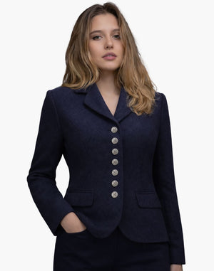 Front view of a woman wearing a deep navy tailored jacket with a notched collar and a vertical row of decorative silver-tone buttons down the front. The fitted jacket features flap pockets at the waist and structured seams for a shaped silhouette, paired with dark trousers. The background is plain light gray.