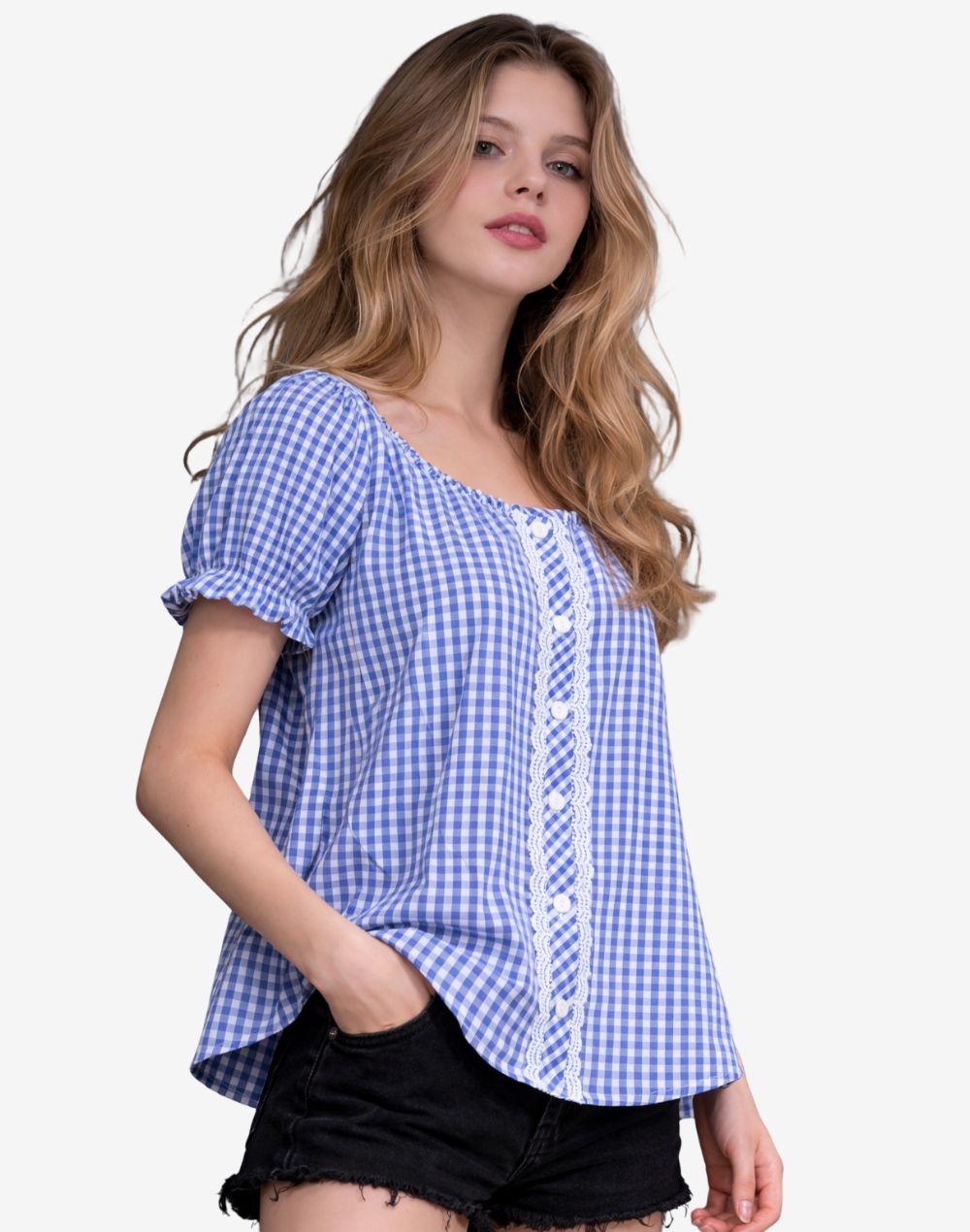 Side angle view of a woman wearing a blue and white gingham dirndl blouse with lace panel detail and short puff sleeves, paired with black denim shorts.