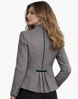 Back view of a woman wearing a tailored grey wool jacket with a fitted silhouette, green trim running vertically down the center back, and pleated detailing at the waist. The jacket features decorative buttons on the sleeves and is paired with dark pants against a plain light background.
