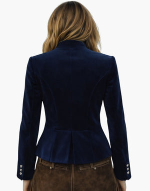 Back view of a woman wearing a premium alpine Trachten jacket in navy blue, structured tailoring, and traditional Bavarian design, paired with brown lederhosen, against a white background.