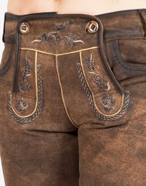 Close-up view of traditional brown leather women’s lederhosen showing decorative front flap with embroidered patterns, metal buttons, and detailed stitching on textured leather.