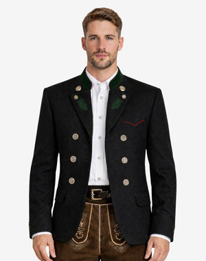 Model wearing alpine black wool men’s Trachten jacket with green collar accents, decorative buttons, and traditional Bavarian design paired with lederhosen.