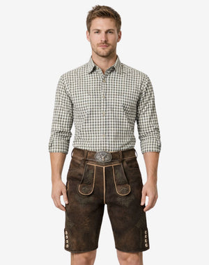Model wearing alpine style lederhosen for men in dark brown leather with Bavarian embroidery and traditional belt buckle
