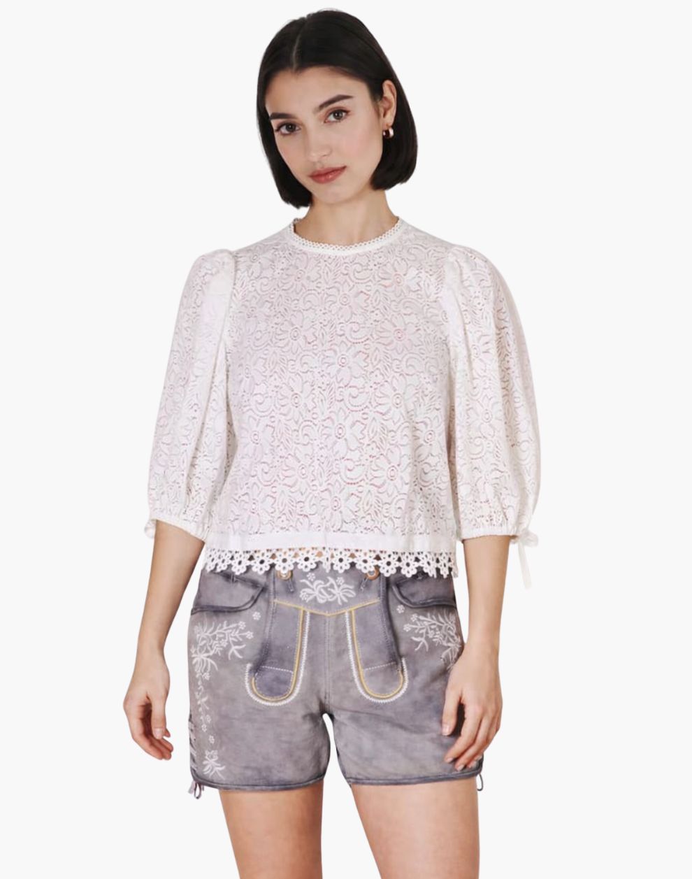 Woman wearing a white lace top and denim shorts on a white background