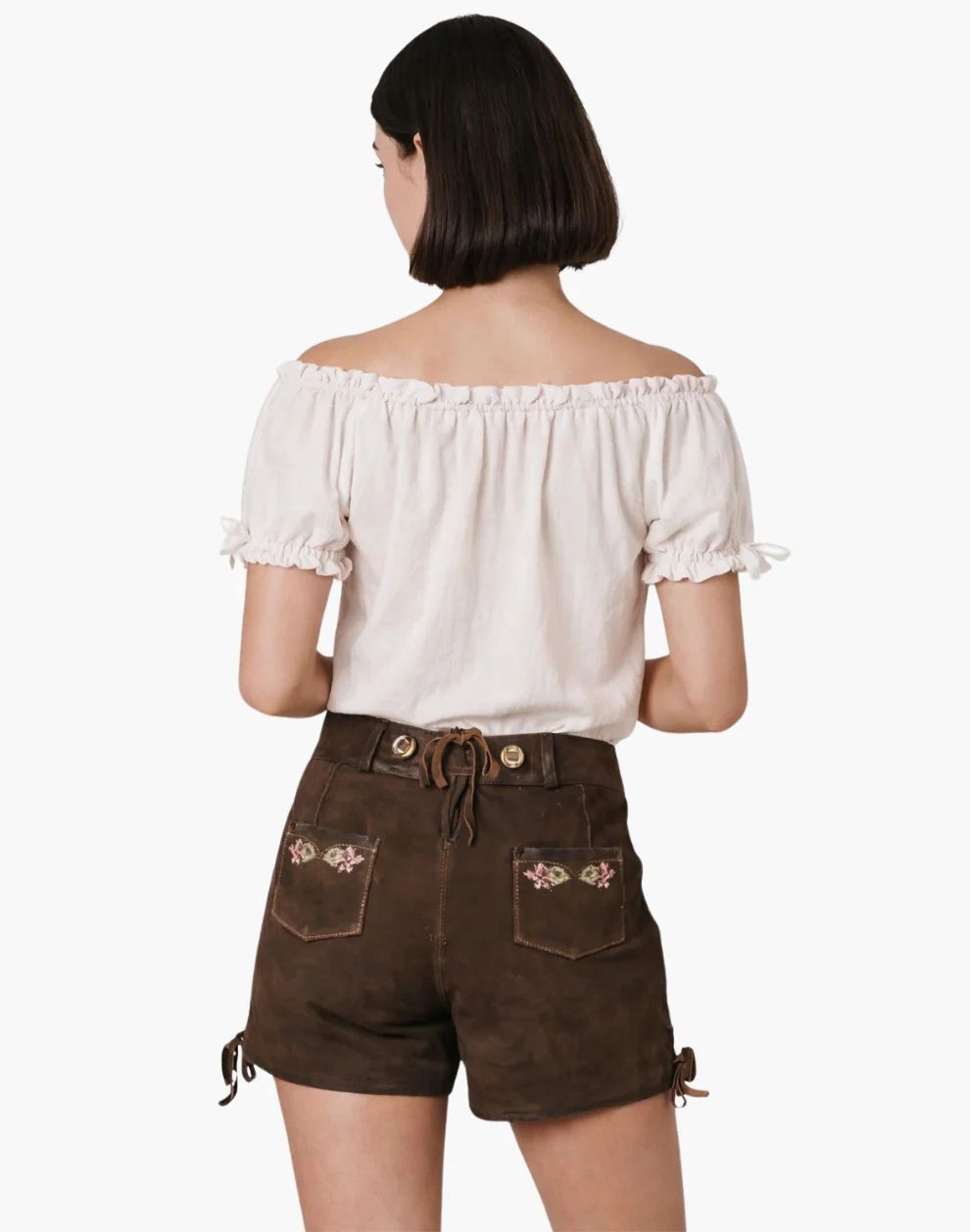 Woman wearing a white off-shoulder top and brown shorts with floral embroidery on a white background