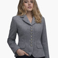 Front view of a woman wearing a light gray tailored jacket with a notched collar and a vertical row of decorative silver-tone buttons down the front. The fitted jacket features flap pockets at the waist and shaping seams for a defined silhouette, paired with dark trousers. The background is plain light gray.