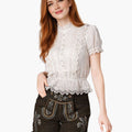 Woman wearing a white lace top and black embroidered shorts on a white background