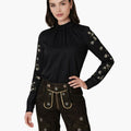 Woman wearing a black long-sleeve top with floral embroidery and black shorts with gold accents on a white background