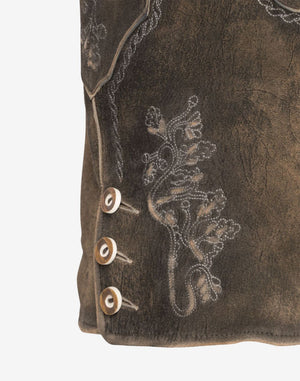 Close-up of brown leather women’s lederhosen leg featuring traditional embroidered floral patterns and decorative side buttons on a distressed leather surface.