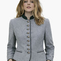 Woman wearing a classic German Trachten jacket in light grey with a green collar, decorative buttons, and fitted traditional Bavarian design, paired with brown lederhosen, against a white background.