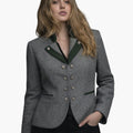 Front view of a woman wearing a tailored gray wool jacket with dark green lapel accents and decorative silver-tone buttons arranged in two vertical rows. The jacket features green-trimmed welt pockets and a fitted silhouette, paired with dark jeans. The background is plain light gray in a clean studio setting.