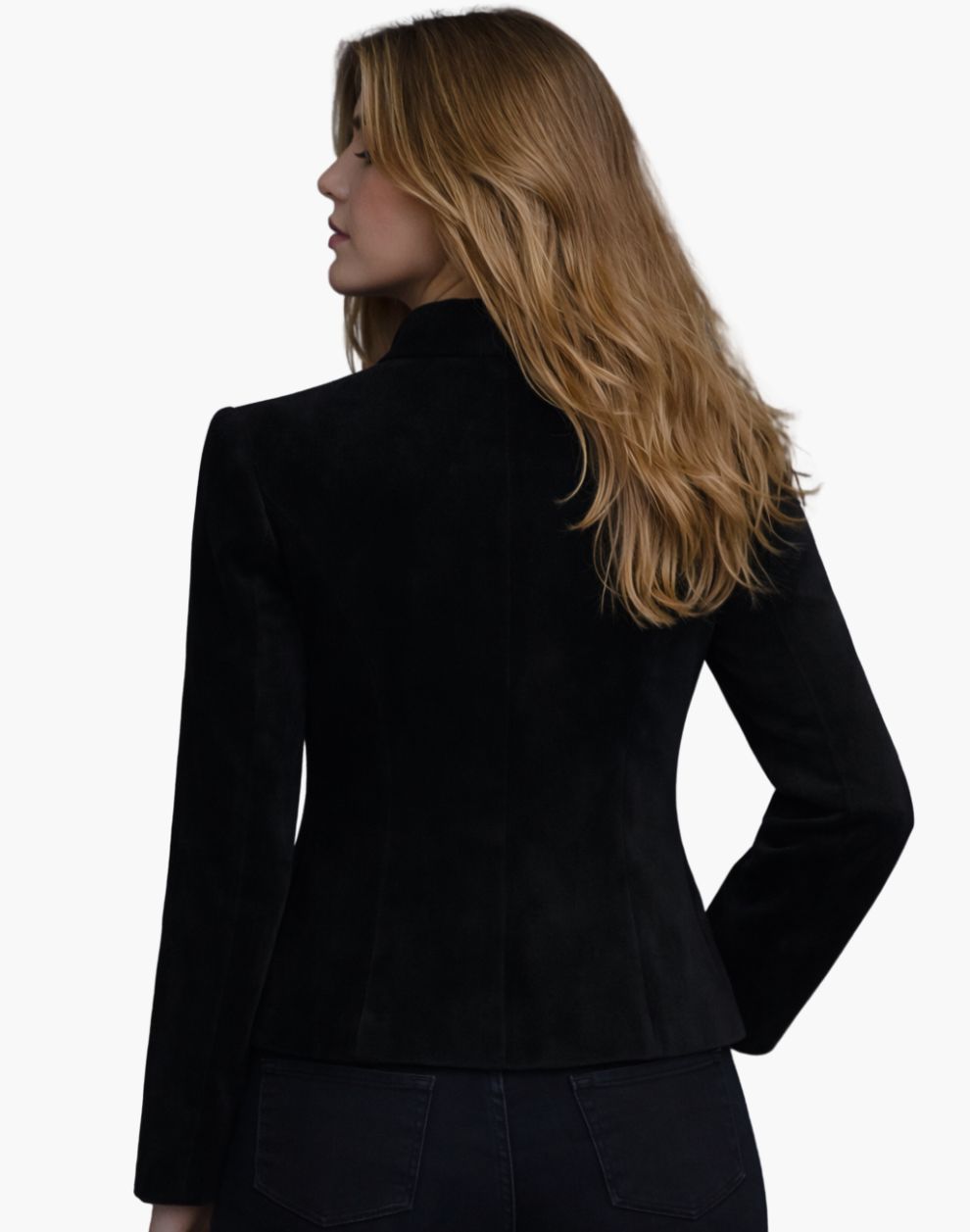 Back view of a woman wearing a fitted black tailored jacket with long sleeves and structured seams that shape the waist. The hem flares slightly over dark jeans, and her shoulder-length blonde hair falls loosely over the collar. The background is plain light gray in a studio setting.