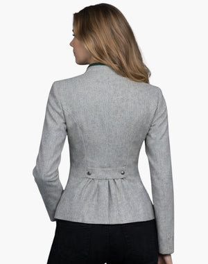 Back view of a woman wearing a fitted light gray wool jacket with structured seams and a peplum-style hem. The jacket features a decorative back tab with two buttons at the waist and soft gathers below it. She pairs it with dark jeans, and her shoulder-length blonde hair falls over a green-trimmed collar. The background is plain light gray in a studio setting.