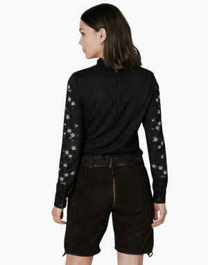 Woman wearing a black long-sleeve top with floral patterns and black shorts on a white background