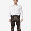 Front view of model wearing genuine leather Bundhosen for men in dark brown with traditional Bavarian embroidery and knee tie detailing for Oktoberfest attire
