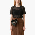 Woman wearing a black sheer top and brown skirt holding a decorative bag on a white background