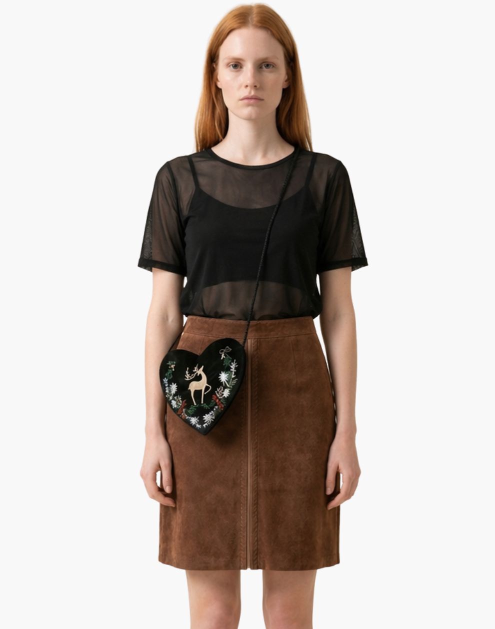 Woman wearing a black sheer top and brown skirt holding a decorative bag on a white background