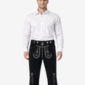 Front view of model wearing mens traditional Bavarian Bundhosen in black leather with embroidered Bavarian motifs and knee-length ties for Oktoberfest style