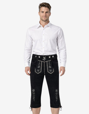 Front view of model wearing mens traditional Bavarian Bundhosen in black leather with embroidered Bavarian motifs and knee-length ties for Oktoberfest style