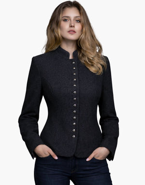 Woman wearing a charcoal grey Trachten-style jacket with decorative buttons, high collar, and a fitted tailored design, paired with dark jeans, against a white background.