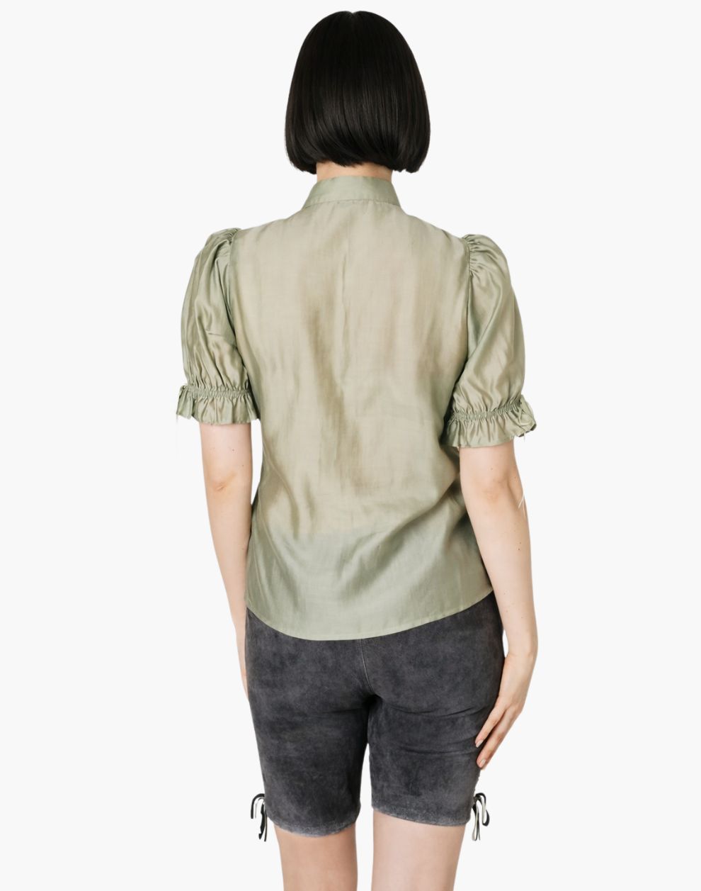Person wearing a light green blouse with puffed sleeves and dark gray shorts on a white background