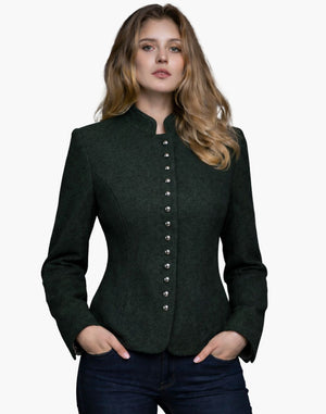 Woman wearing a dark green Trachten-style jacket with decorative buttons, high collar, and a fitted tailored design, paired with dark jeans, against a white background.