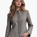 A young woman wearing a fitted grey wool jacket with decorative metal buttons down the front and green trim along the edges. The jacket has a structured, tailored shape, and she pairs it with black pants while standing against a plain light background.