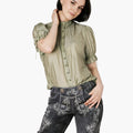 Woman wearing a green blouse and dark denim shorts with floral embroidery on a white background