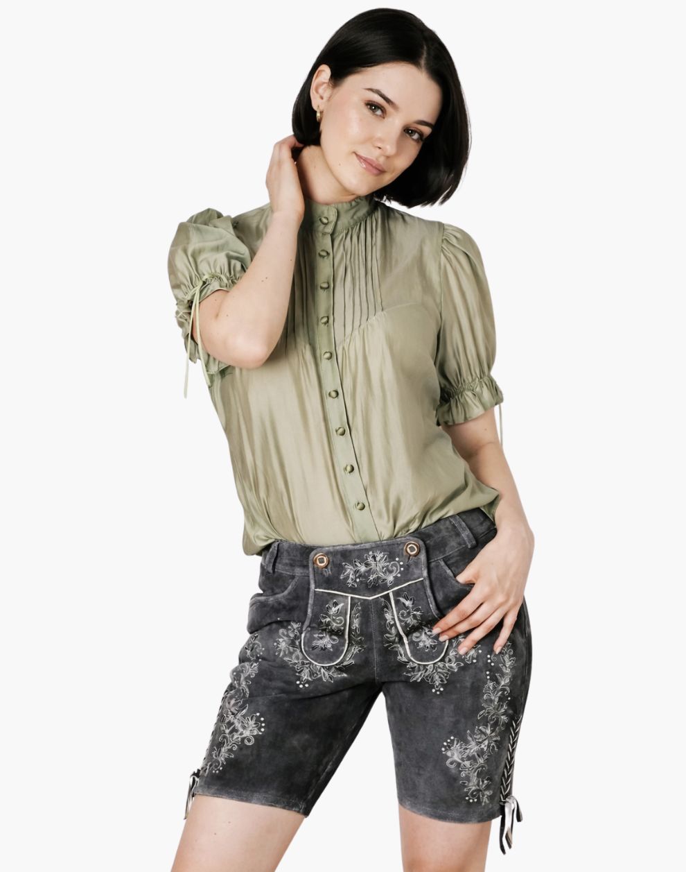 Woman wearing a green blouse and dark denim shorts with floral embroidery on a white background