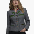 Front view of a woman wearing a gray wool jacket with green decorative trim and leaf-shaped appliqué details on the chest. The jacket has a stand-up collar with red, white, and green accents, a row of decorative buttons down the front, and green-trimmed welt pockets. She is styled with dark jeans. The background is plain light gray, creating a clean studio look.