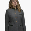 Front view of a woman wearing a charcoal gray tailored jacket with a stand-up collar trimmed in dark green. A vertical row of small metallic buttons runs down the front, and the fitted silhouette is styled with dark jeans. The background is plain light gray.