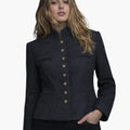 Front view of a woman wearing a dark charcoal tailored jacket with a stand-up collar and a vertical row of decorative gold-tone buttons down the front. The jacket features subtle welt pockets and structured seams that shape the waist, paired with dark jeans. The background is plain light gray in a clean studio setting.