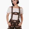 Female model wearing brown embroidered lederhosen with suspenders and an off-shoulder white blouse, styled in traditional Bavarian Oktoberfest fashion.