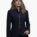 Front view of a woman wearing a navy tailored blazer with a stand-up collar and a row of decorative metal buttons down the front. The fitted jacket has long sleeves and a slightly flared hem, styled with dark jeans. The background is plain light gray, giving the image a clean studio look.
