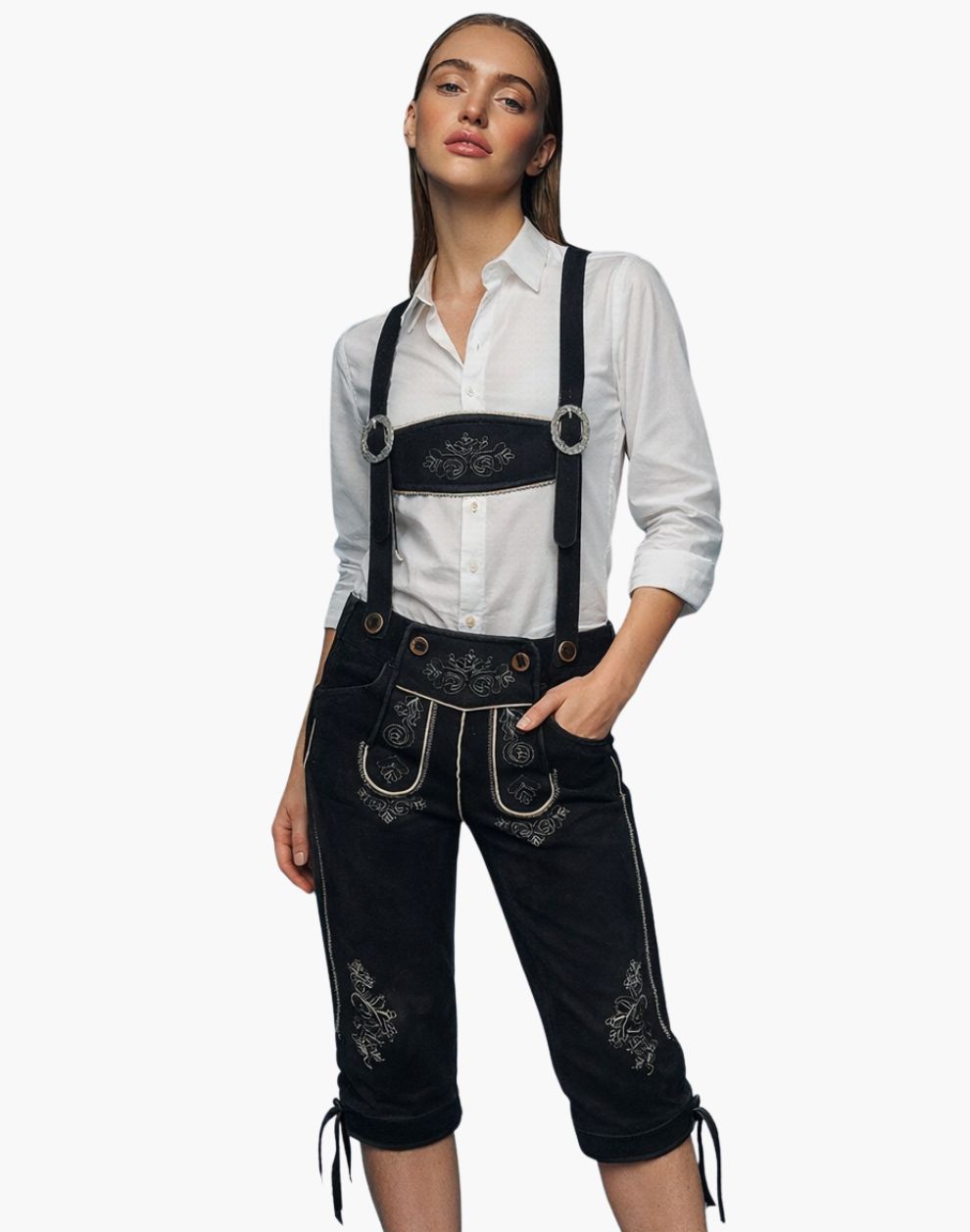 Woman wearing black embroidered lederhosen with a white shirt on a white background